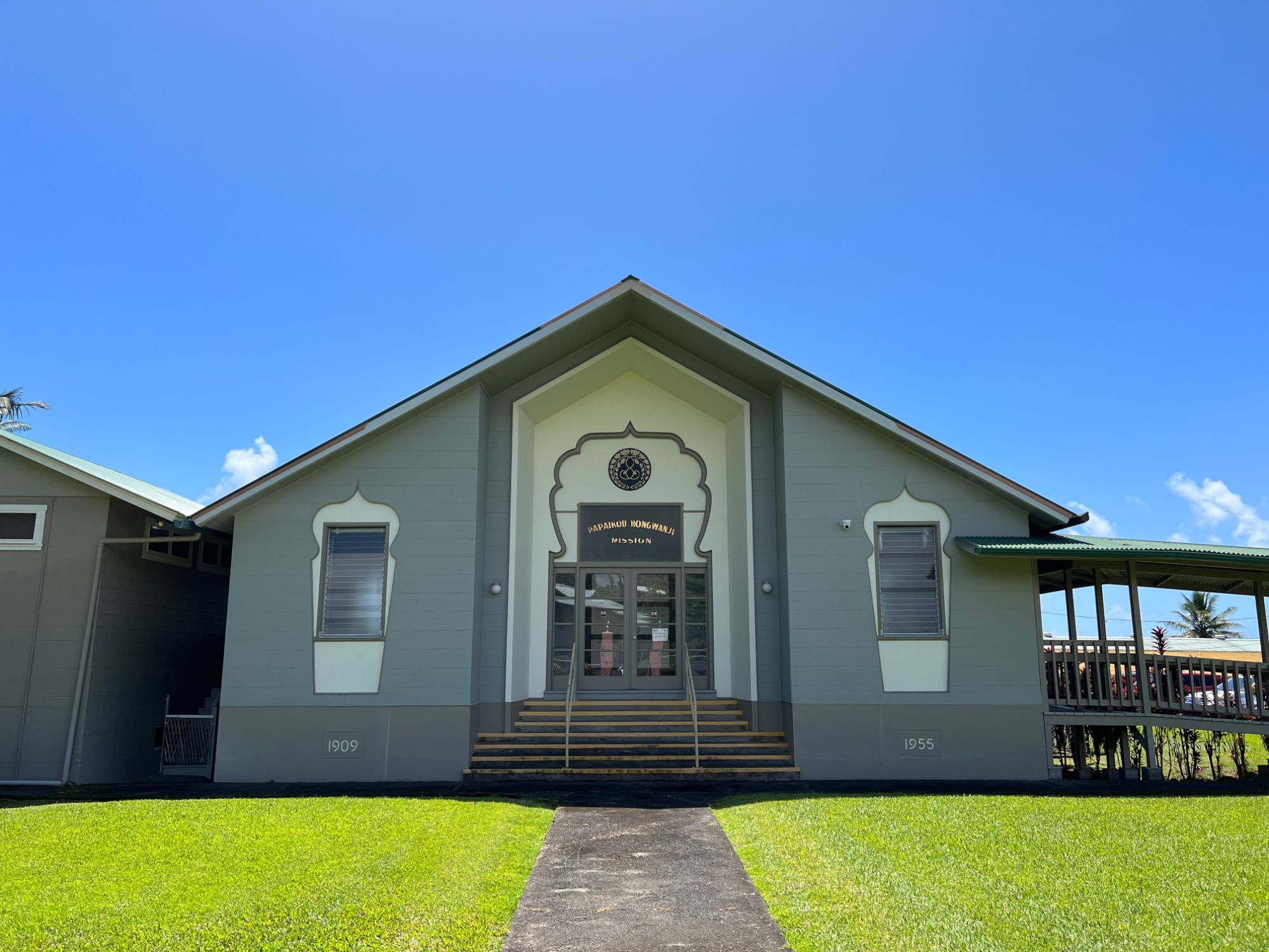 Front of Papaikou Hongwanji Mission, a gray-green temple building with a cream arched entrance and the temple crest above the doors