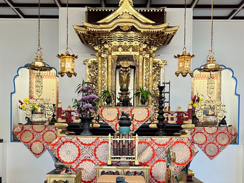 The altar of Papaikou Hongwanji Mission: a gilded shrine with a standing image of Amida Buddha at the center, hanging lanterns, flowers, and red and gold altar cloths.